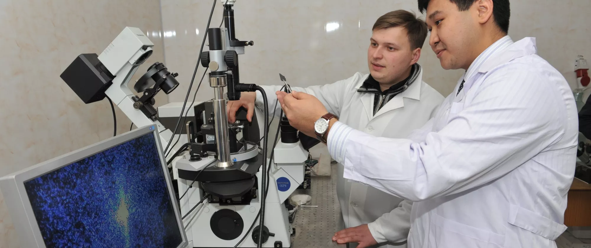 Two men in white coats work at a state-of-the-art microscope.