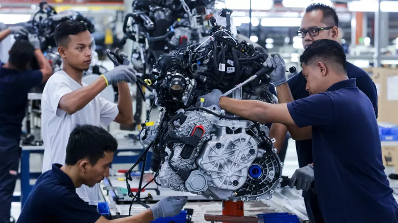 Workers in a Malaysian Car factory work on an engine