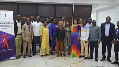 Participants pose in colourful dresses and formal attire, standing next to a banner with the name of the project